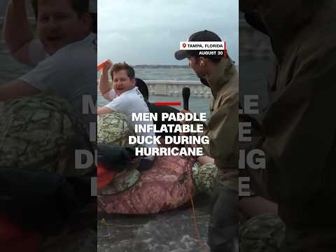 Men paddle inflatable duck during hurricane
