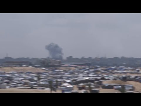 Displaced people at Israel-declared humanitarian zone, smoke plume rises in distance